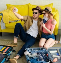 beautiful couple taking selfie on smartphone while packing suitcases for vacation